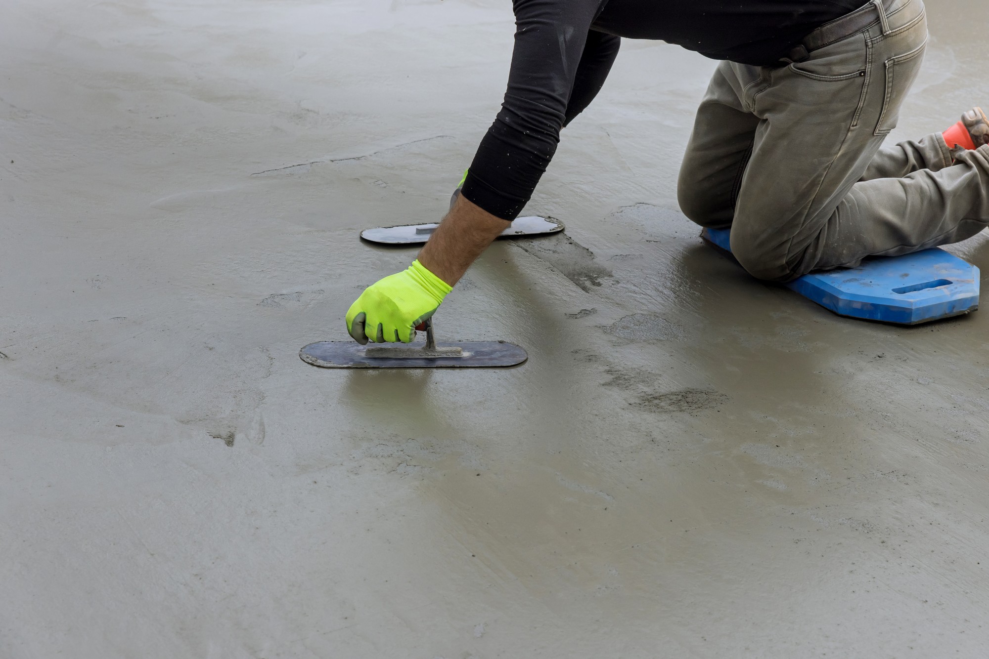 Sure! Here is an example of a detailed alt text description for the image from the given URL:
"A masonry worker wearing a white shirt and blue overalls is holding a steel trowel in their right hand. They are in the process of smoothing out the surface of a freshly applied layer of plaster on a concrete wall. The worker has a focused expression, and their hands are slightly dusty from the material. The background shows an unfinished construction site, with scaffolding and other building materials such as bags of plaster and buckets. The lighting is natural, indicating that the work might be taking place during the daytime. The steel trowel in their hand has residual wet plaster on its blade, reflecting the ongoing nature of the task."
Feel free to adjust the description based on any additional details or context about the image!