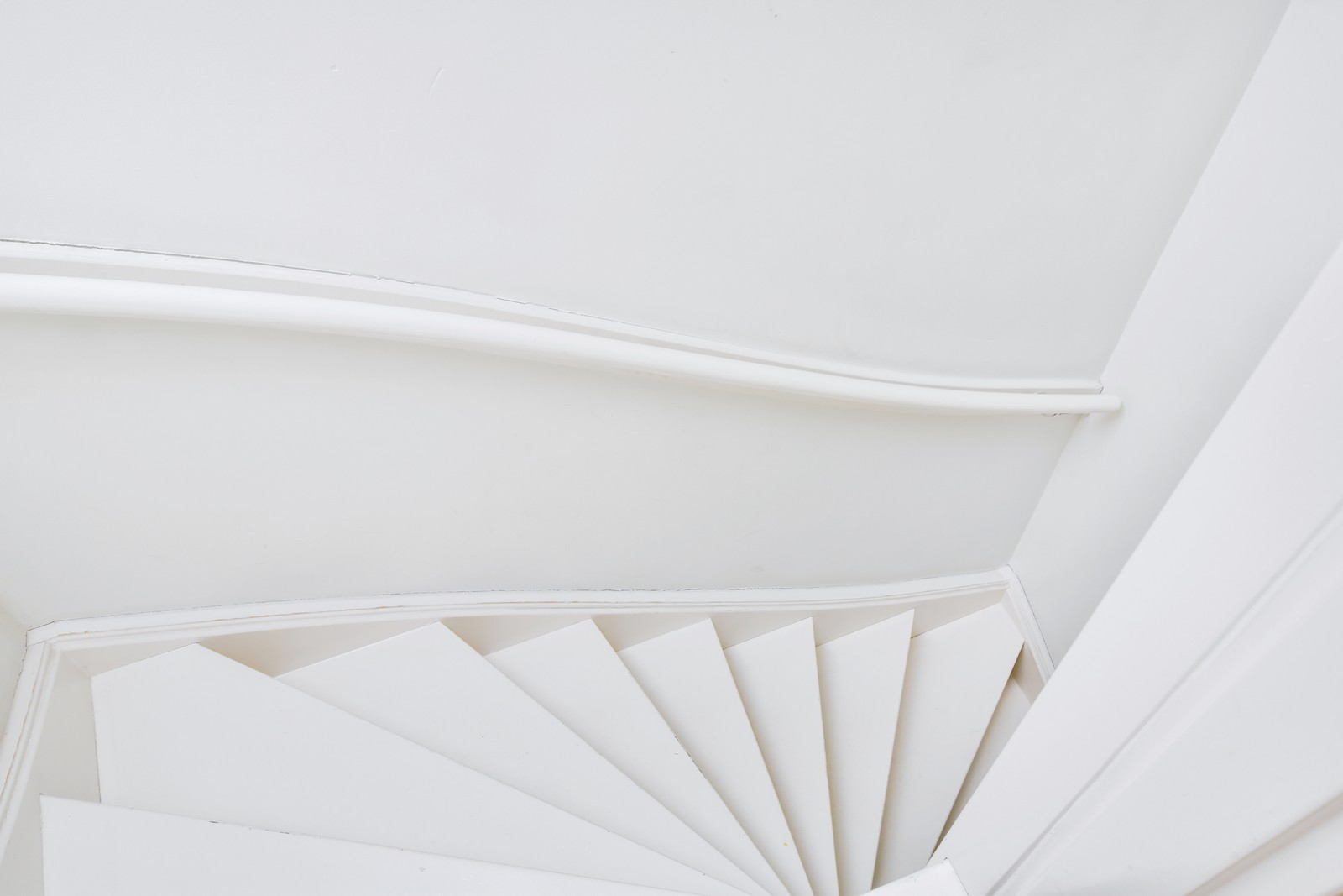 The image features a sleek, modern spiral staircase in a contemporary flat. The staircase is painted in a pristine white colour, contributing to a clean and minimalist aesthetic. It ascends gracefully in a helical form, with each step seamlessly flowing into the next. The staircase's design incorporates smooth, rounded edges and a uniform, continuous railing that follows the curvature of the spiral.
The backdrop of the flat includes smooth, white walls and a light, neutral-toned floor, which together enhance the bright and airy feel of the space. Large floor-to-ceiling windows in the room allow an abundance of natural light to flood in, creating a luminous and open environment. The overall decor of the flat is minimal, focusing on simplicity and elegance, with subtle elements that underscore the modern design theme.
This image captures the staircase as a central feature in the flat, highlighting both its functional role and its contribution to the aesthetic appeal of the living space.